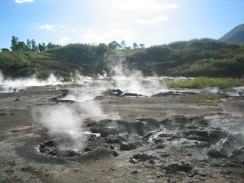 Steam rises from bubbling volcanic mud pools at the foot of Cerro Negro, where geothermal activity meets rugged black earth in a stark and other-worldly landscape.
